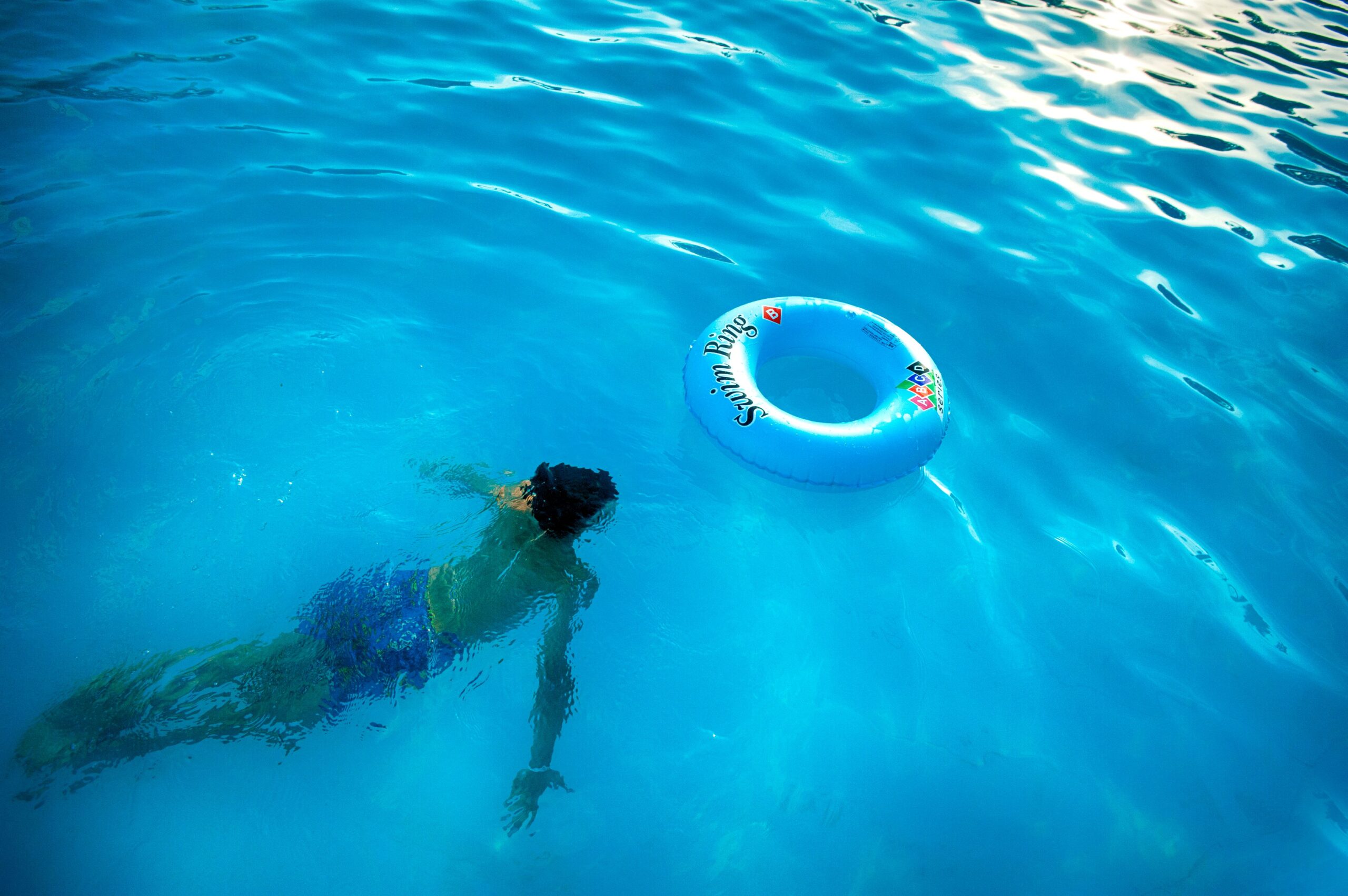  Overhead view of a man enjoying a swim in a blue swimming pool with a floating inflatable ring.