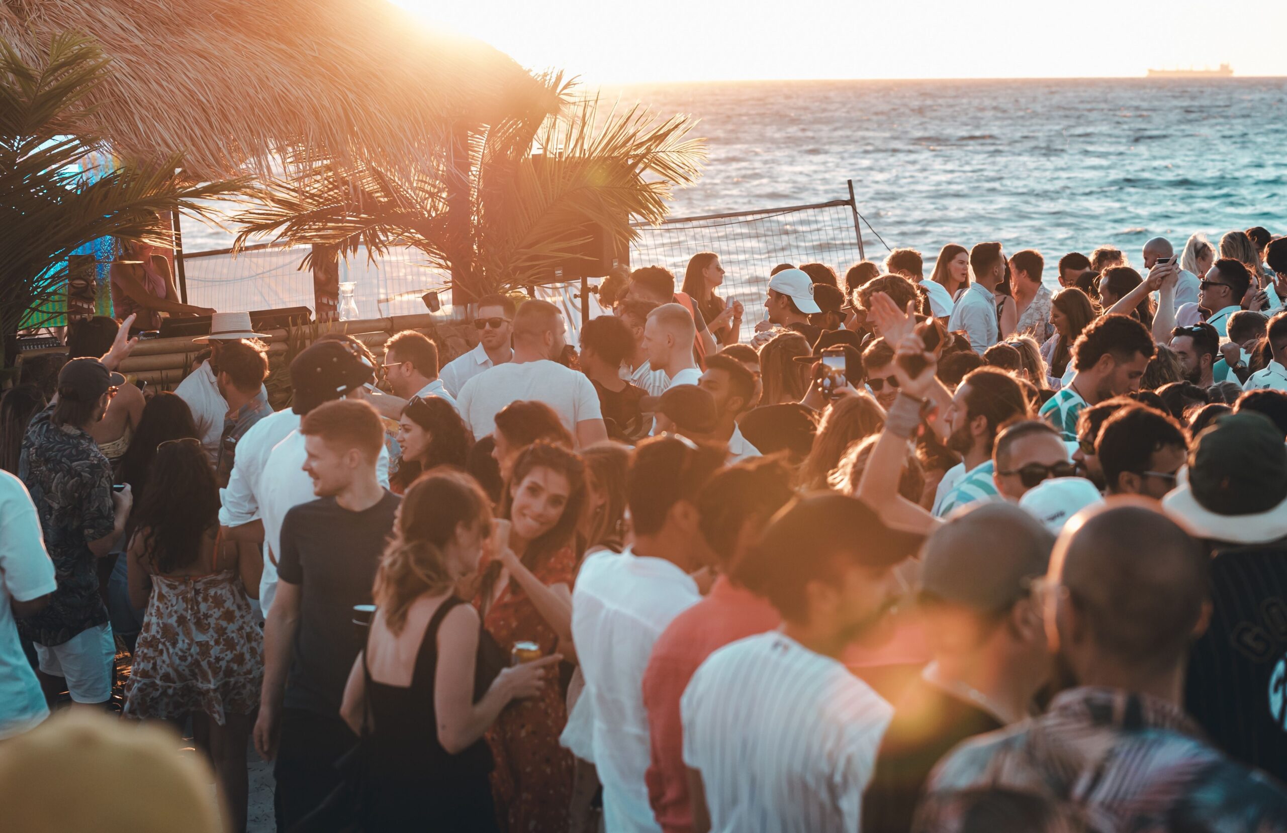Crowded beach party with many people gathered along the shoreline.