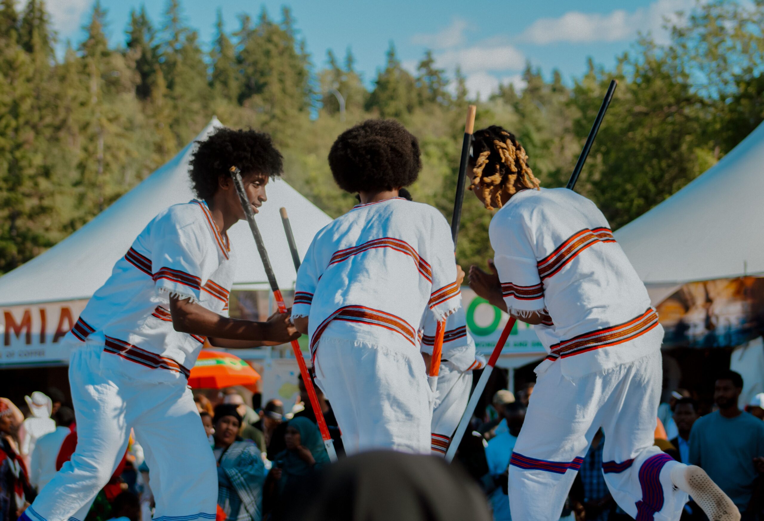 Three young people wearing traditional white attire, dancing together at a cultural festival.