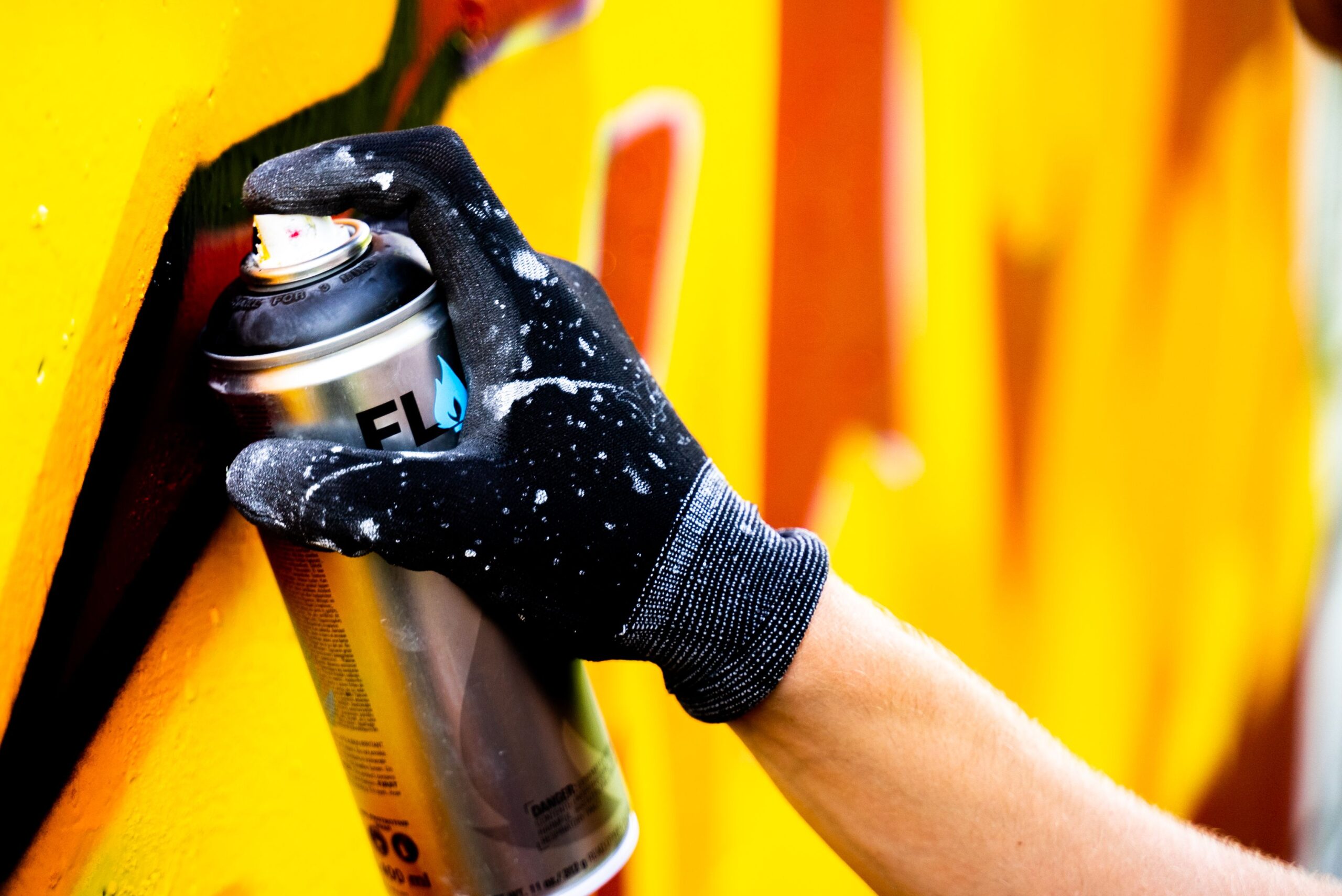 Close-up of a hand using spray paint to create graffiti artwork on a wall.