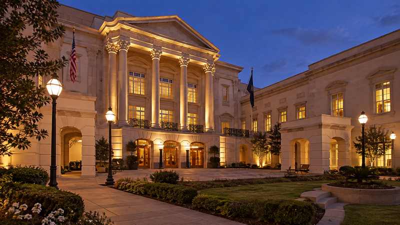 Illuminated neoclassical performing arts building and courtyard at dusk.