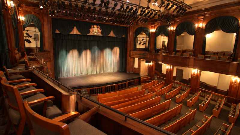 Historic theater interior with wooden seating, balconies, and a stage.