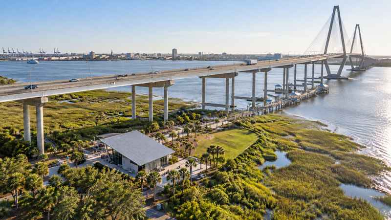 Aerial view of Mount Pleasant Memorial Pier beside the Arthur Ravenel Jr. Bridge, with waterfront marshes and Charleston Harbor.