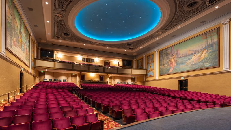 Alt Text: Interior of the Sottile Theatre in Charleston, featuring red theater seats, decorative wall murals, and a blue illuminated ceiling.